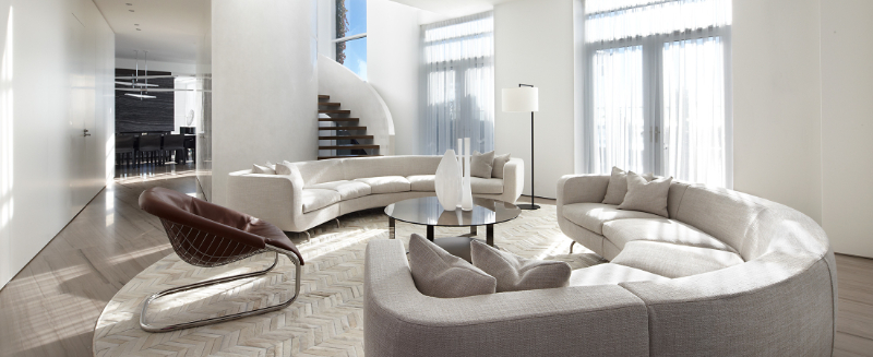 Modern Sofa Design by Studio Munge. This neutral living room has two white sofas, one armchair in brown, a center table between the sofas and covering all the room is a round neutral rug.